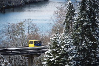 The PRT in Morgantown traveling in front of the river with snow on the surrounding trees.